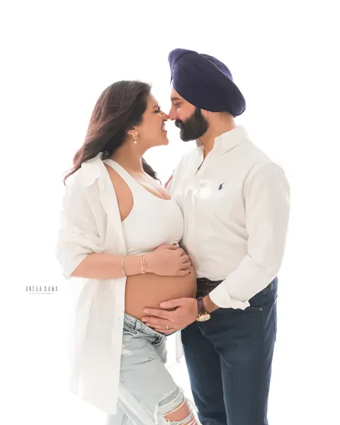 Pregnancy photoshoot in Delhi: couple touching noses, husband in a navy turban and white shirt and wife in an open white shirt and jeans