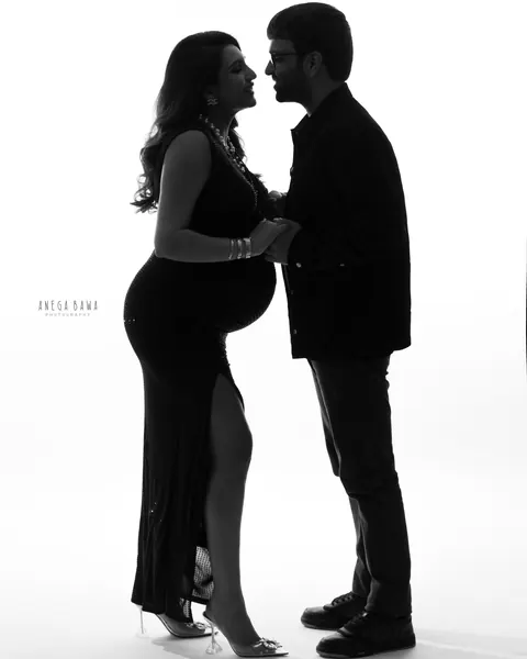 Pregnancy photoshoot in Delhi: backlit black and white silhouette of a couple holding hands and smiling at each other, wife in a black