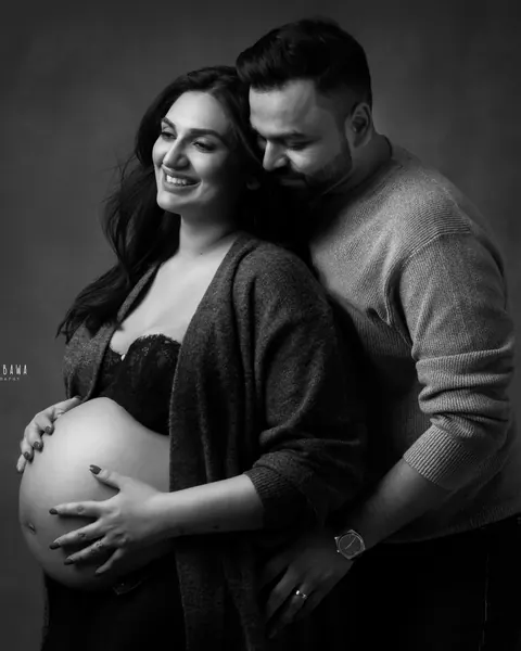 Pregnancy photoshoot in Delhi: black and white portrait of a husband hugging his wife from behind, she wears an open cardigan with her bare