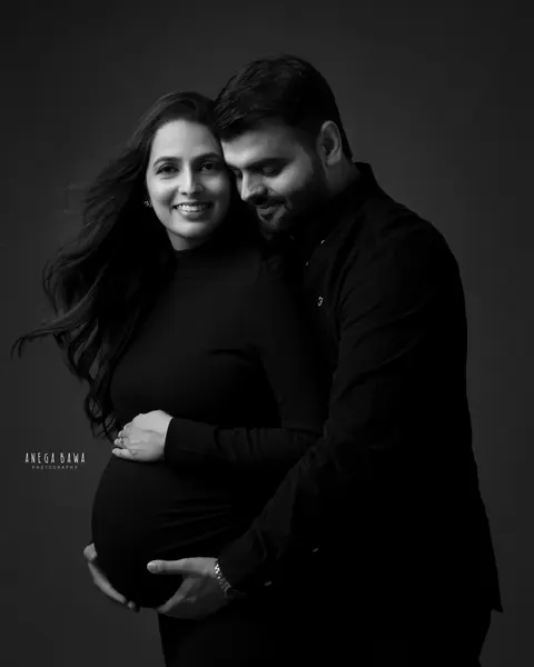Pregnancy photoshoot in Delhi: black and white portrait of a smiling couple in black, husband hugging his wife from behind with his hands