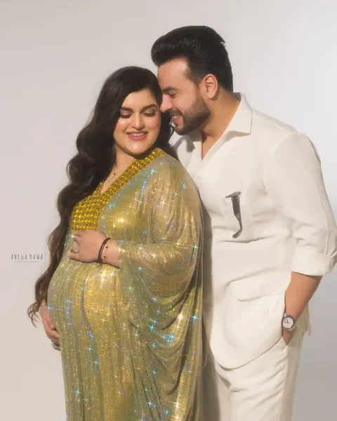 Pregnancy photoshoot in Delhi: husband in an all-white outfit nuzzling his smiling wife who wears a sparkling gold crystal kaftan gown, her