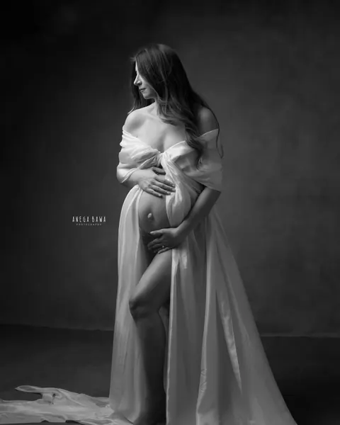Pregnancy photoshoot in Delhi: black and white portrait of expecting mother wrapped in flowing silk, looking to the side with hands on her