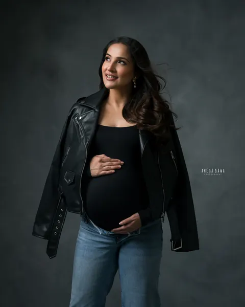 Pregnancy photoshoot in Delhi: expecting mother in a black bodysuit and jeans with a black leather jacket draped over her shoulders