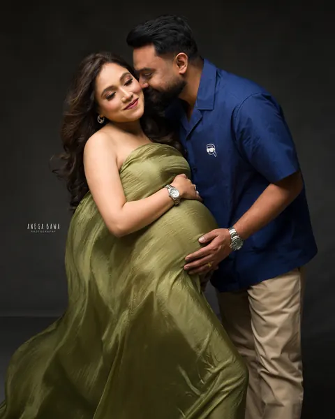Pregnancy photoshoot in Delhi: expecting mother in an olive green satin drape with her husband in a navy shirt kissing her cheek, dark