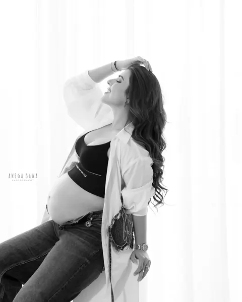 Pregnancy photoshoot in Delhi: black and white portrait of expecting mother seated in an open white shirt and jeans, one hand in her hair