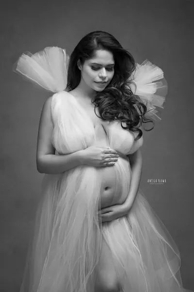 Black and white portrait of expecting mother in a tulle gown with oversized puffed tulle shoulders, open front, hands cradling her bare