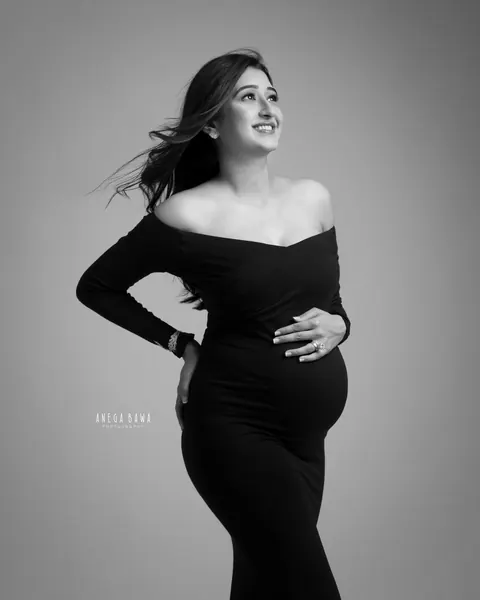 Pregnancy photoshoot in Gurgaon: black and white portrait of expecting mother in an off-shoulder black gown looking upward with windswept