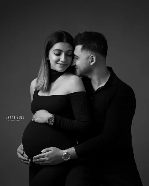 Pregnancy photoshoot in Gurgaon: black and white portrait of a couple cheek to cheek, wife in a black knit off-shoulder top and husband in