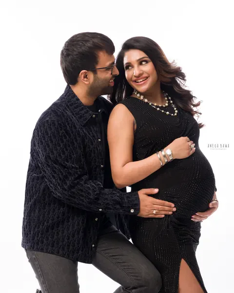 Pregnancy photoshoot in Gurgaon: laughing couple, wife in a black studded dress with pearl necklaces and husband in a dark textured jacket