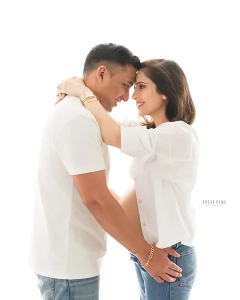 Pregnancy photoshoot in Gurgaon: couple touching foreheads and smiling, wife in a white shirt and light denim, husband in a white tee