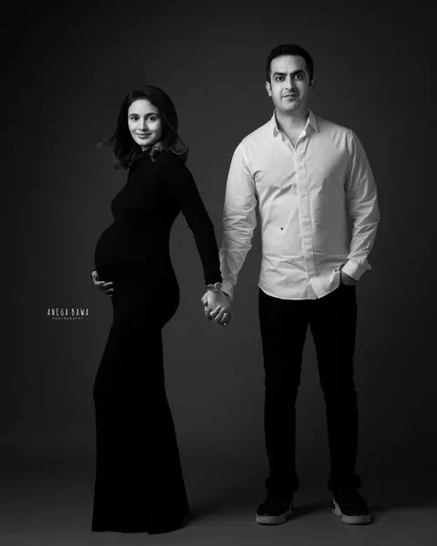 Pregnancy photoshoot in Gurgaon: black and white portrait of a couple standing apart holding hands, wife in profile in a black gown and