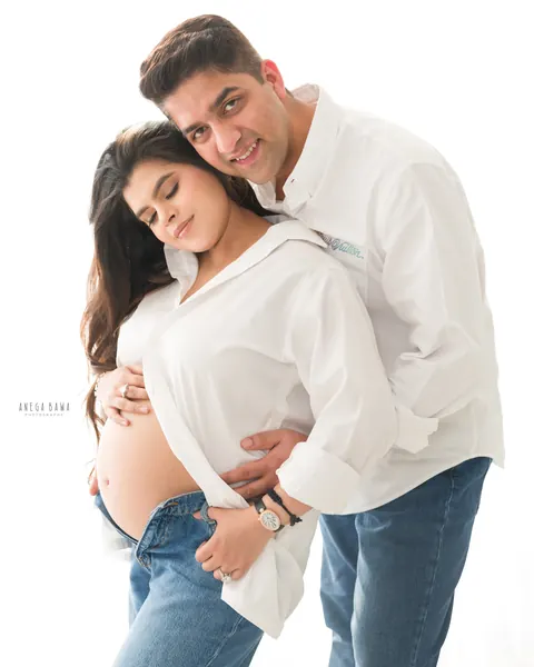 Pregnancy photoshoot in Gurgaon: smiling couple in matching white shirts and jeans, wife resting her head against her husband, hands on her