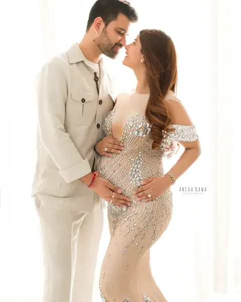 Pregnancy photoshoot in Gurgaon: couple touching noses, wife in a crystal-embellished nude gown and husband in a cream linen jacket and