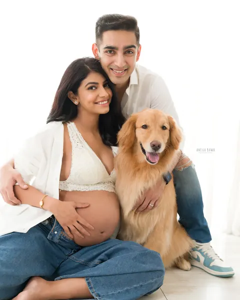 Pregnancy photoshoot in Gurgaon: couple seated on a white floor with their golden retriever, wife in a lace bralette, open white shirt and