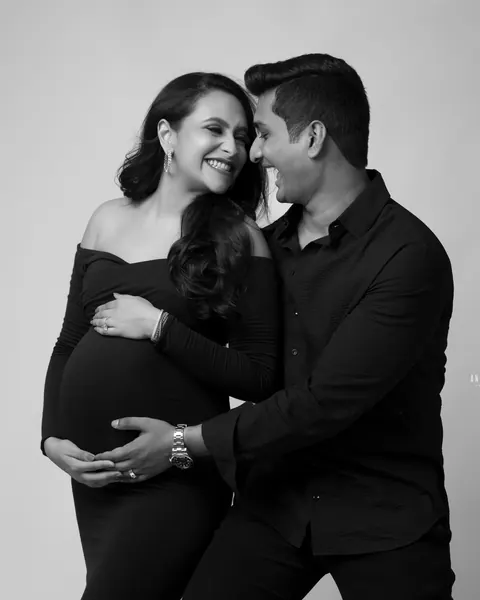 Pregnancy photoshoot in Gurgaon: black and white portrait of a couple laughing together, wife in an off-shoulder black gown and husband in