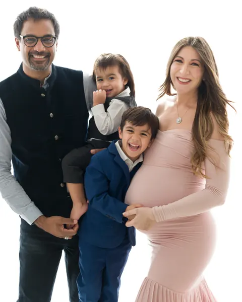 Pregnancy photoshoot in Gurgaon: laughing family with two young sons, expecting mother in a blush pink off-shoulder gown, white backdrop