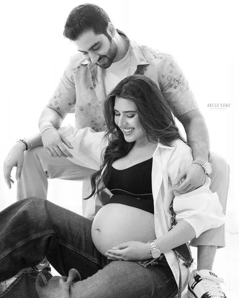 Pregnancy photoshoot in Gurgaon: black and white portrait of a husband seated behind his laughing wife as they both look down at her bare