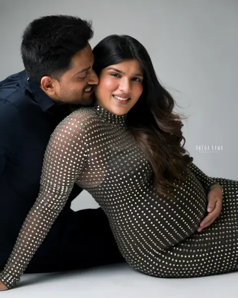 Pregnancy photoshoot in Gurgaon: smiling expecting mother reclining in a crystal-studded gown while her husband in a navy shirt nuzzles her