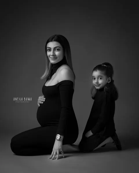 Pregnancy photoshoot in Gurgaon: black and white portrait of expecting mother kneeling in a black knit outfit with her young daughter