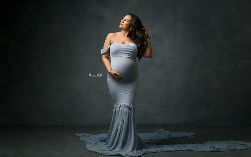 Pregnancy photoshoot in Gurgaon: expecting mother in a powder blue off-shoulder mermaid gown with a long sheer train, looking up with a
