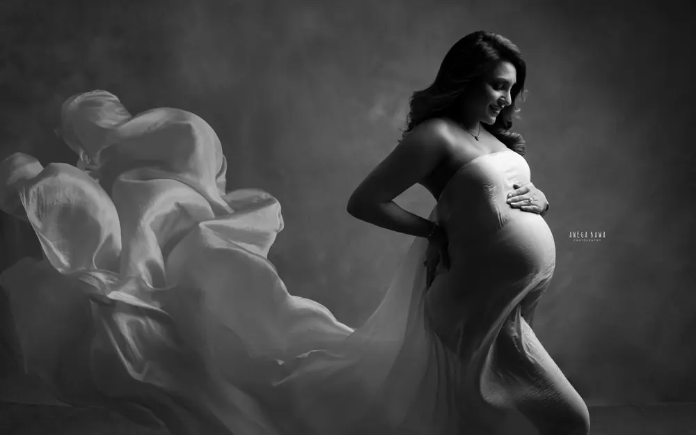 Pregnancy photoshoot in Gurgaon: black and white portrait of a smiling expecting mother in a strapless silk drape with flowing fabric