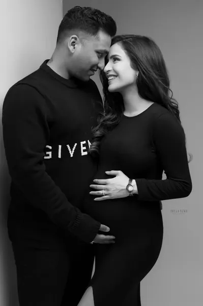 Black and white couple portrait: husband in a black sweatshirt touching foreheads with his smiling wife in a black long-sleeve fitted