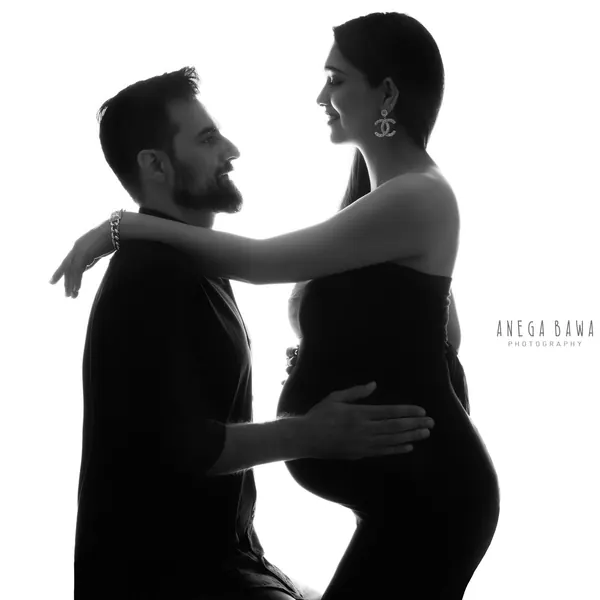 High-key silhouette of a couple facing each other, wife in a black strapless gown with statement earrings, husband in a dark tee and beard