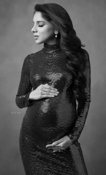 Black and white portrait of expecting mother in a black sequin high-neck long-sleeve fitted gown with pearl drop earrings, eyes down, long
